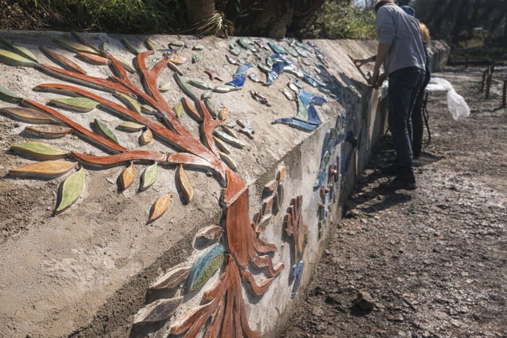 Fresque murale colorée en céramique représentant un arbre et des oiseaux, réalisée en extérieur par plusieurs personnes